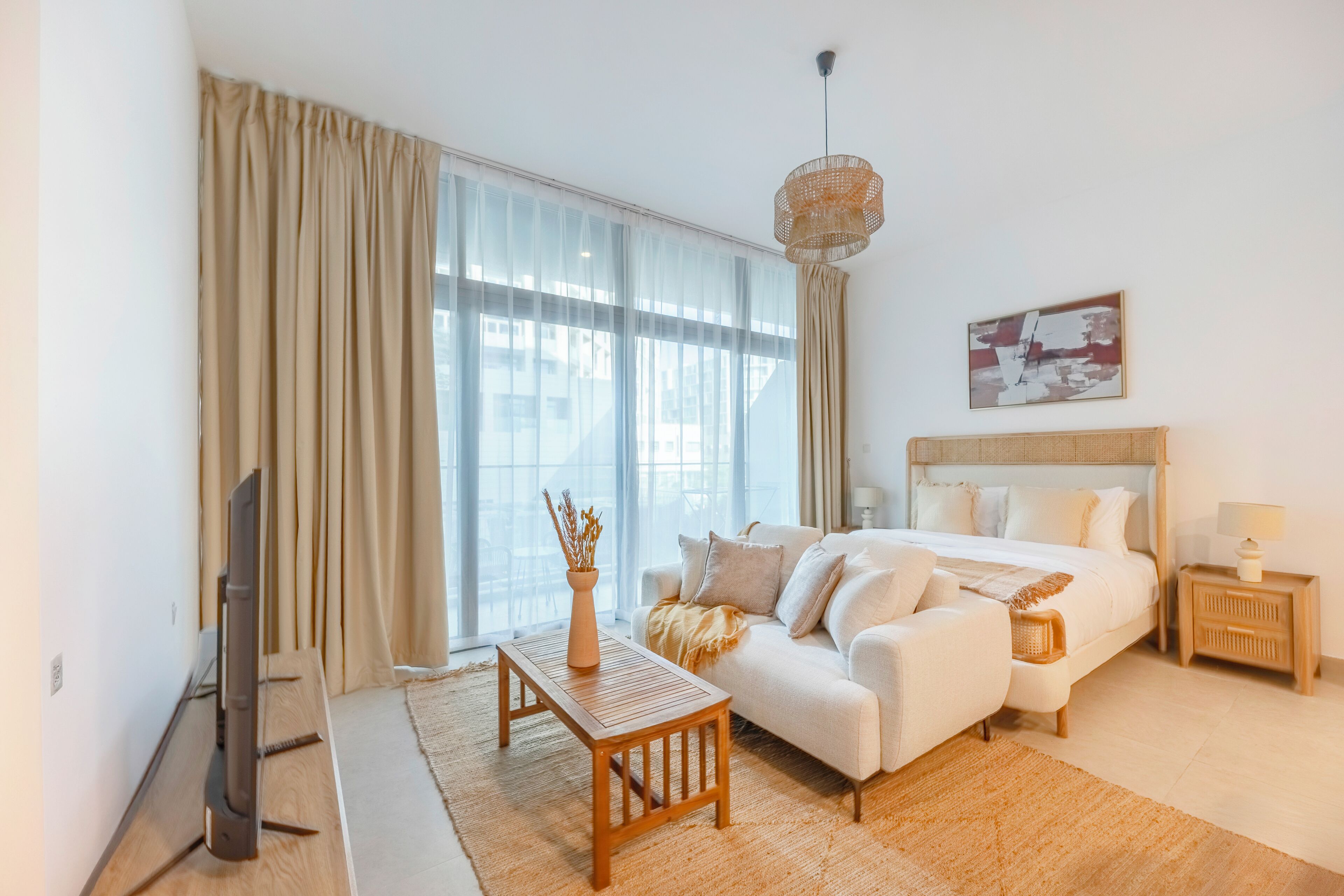 Habitación de hotel moderna con cama, sofá, televisor y un amplio ventanal con cortinas.