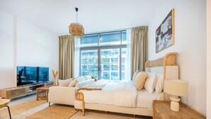 A modern bedroom with a large window, a bed, a TV, and a bedside table. - Bloomfields Studio in Park View   (Abu Dhabi)