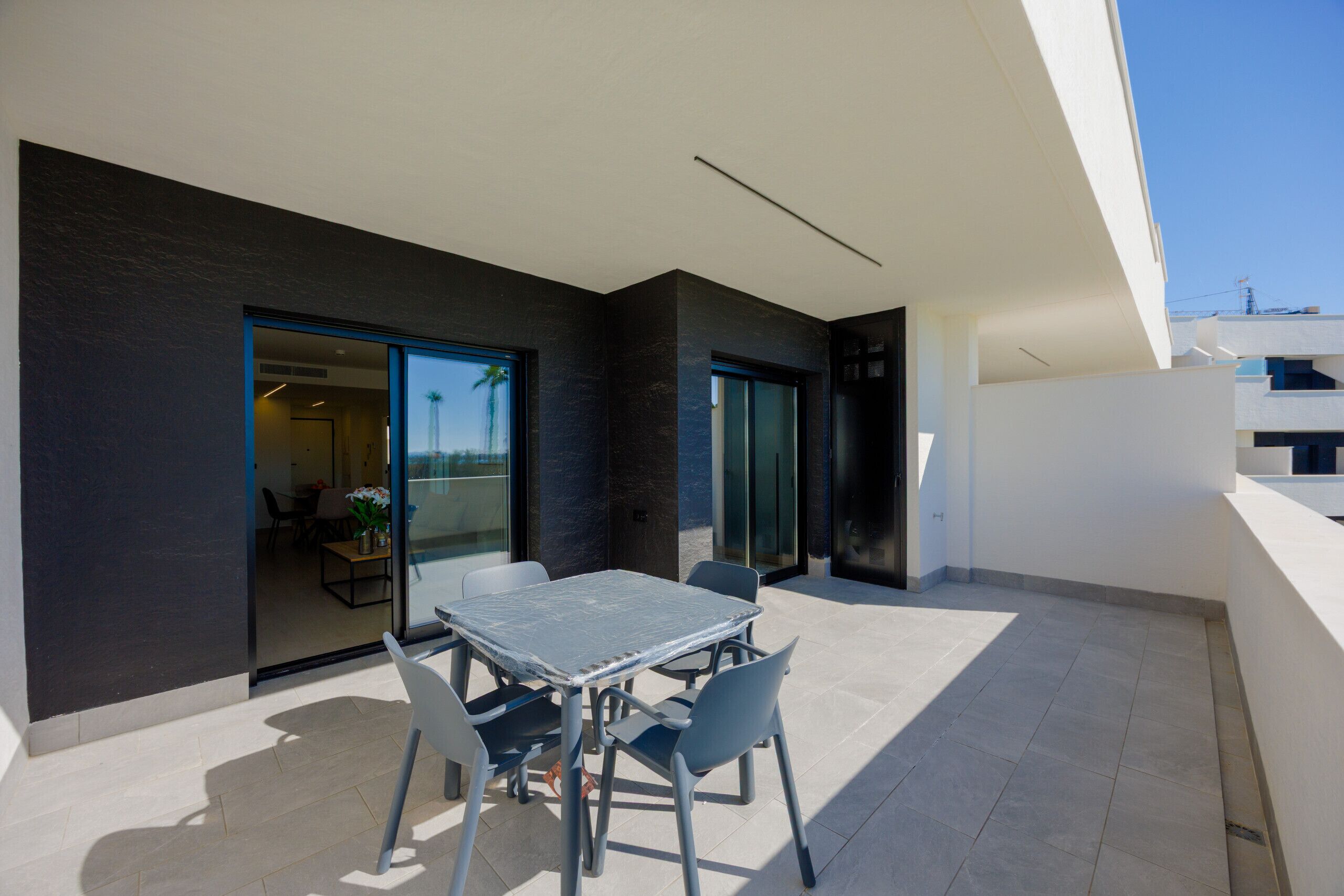 A modern outdoor patio with a table and chairs, a glass door leading to an interior space, and a clear sky.