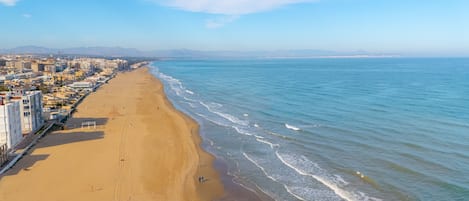 Un paisaje urbano costero con una amplia playa de arena, cielo azul despejado y mar tranquilo.