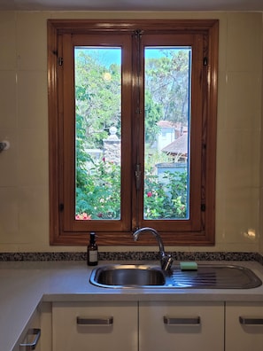 A kitchen with a double wooden-framed window, a stainless steel sink, and a bottle of hand soap. - Charming Guest House with a Private Pool near Gandia (Marxuquera)