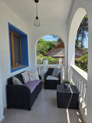 A covered outdoor seating area with a sofa and chairs, a potted plant, and a view of a wooden building. - Charming Guest House with a Private Pool near Gandia (Marxuquera)