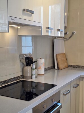 A kitchen with white cabinets, a stainless steel range, a wooden cutting board, and a paper towel holder. - Charming Guest House with a Private Pool near Gandia (Marxuquera)