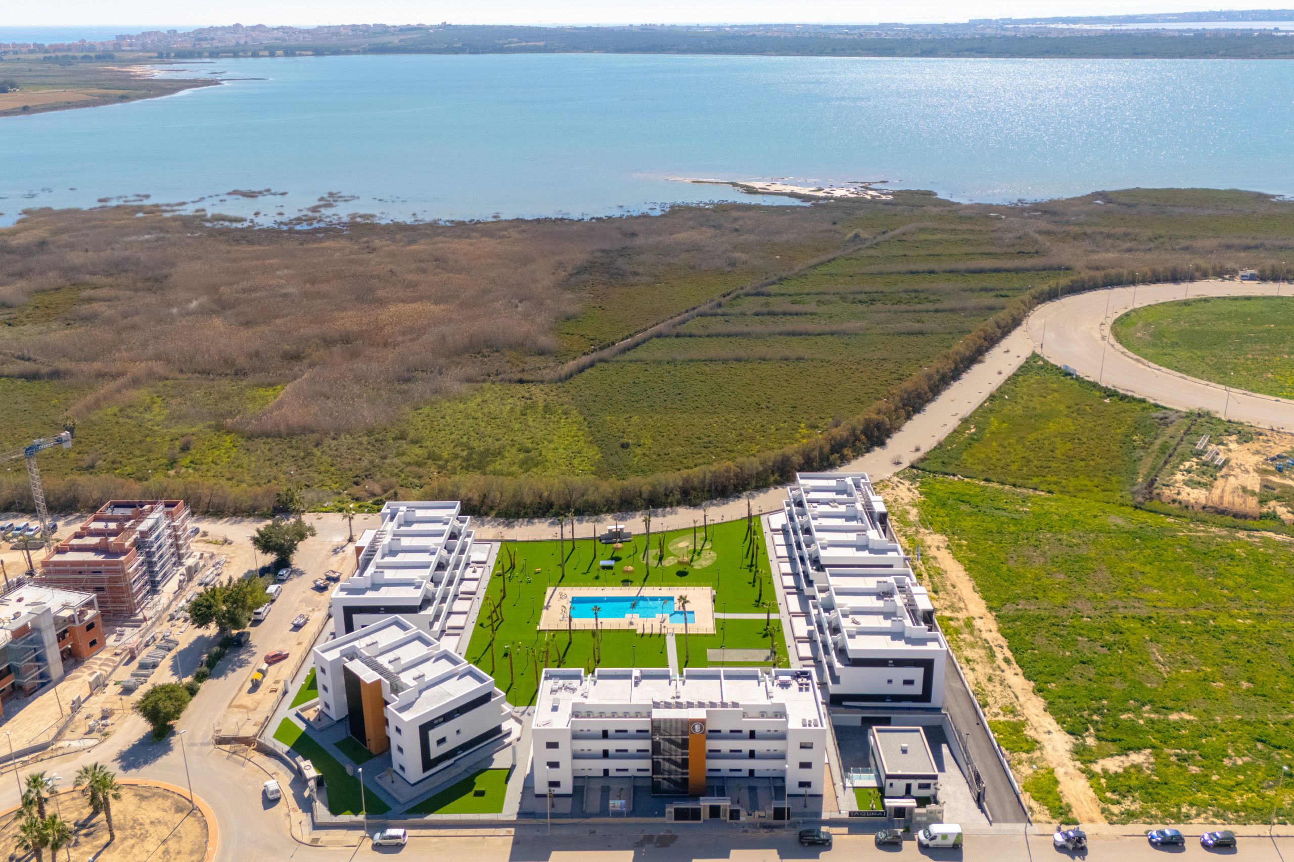Vista aérea de un hotel moderno con piscina, rodeado de vegetación y una masa de agua.