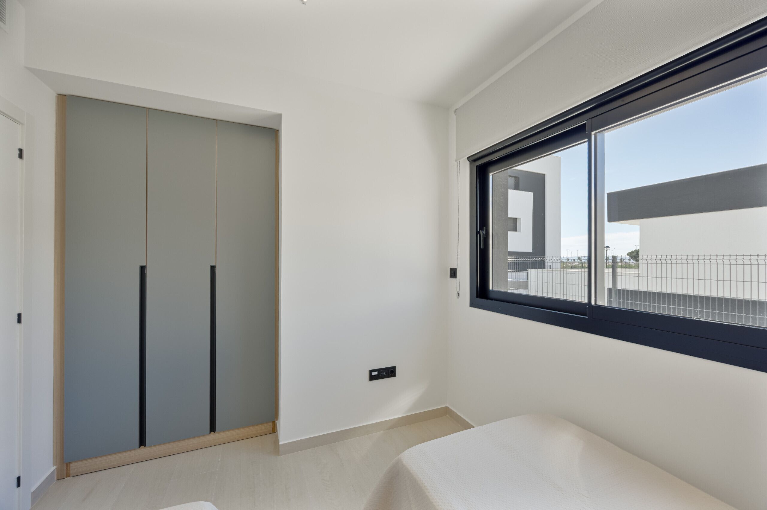 A modern room with a large window, a wardrobe, and a bed.