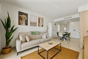 Ein modernes Wohnzimmer mit einer Couch, einem Esstisch, Stühlen, einer großen Pflanze und Kunstwerken an den Wänden.