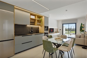 Eine moderne Küche mit integrierten Geräten, ein Essbereich mit einem Glastisch und ein Wohnbereich mit einer Couch und einem Fernseher.