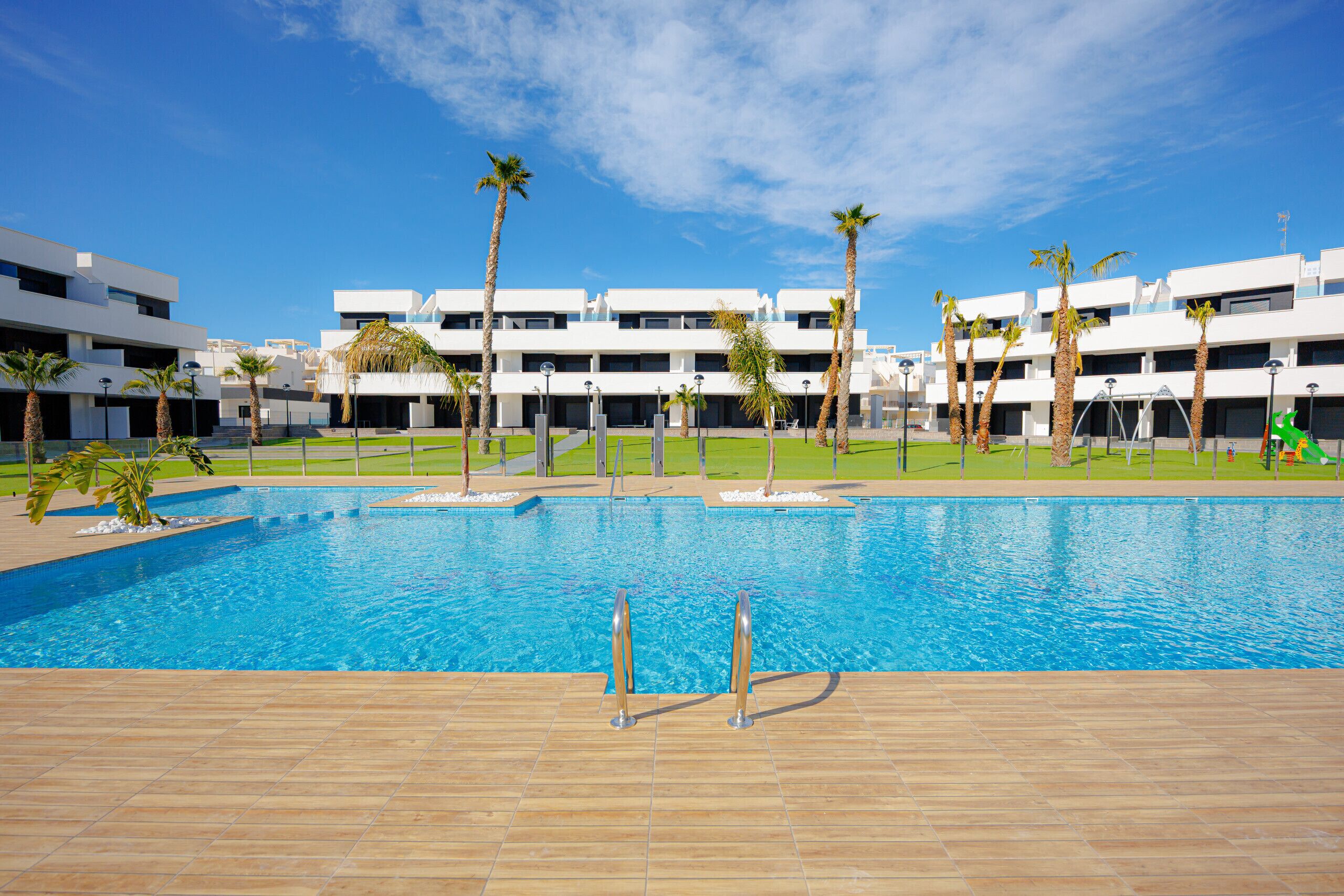 A swimming pool with a tiled deck, surrounded by palm trees and modern buildings.