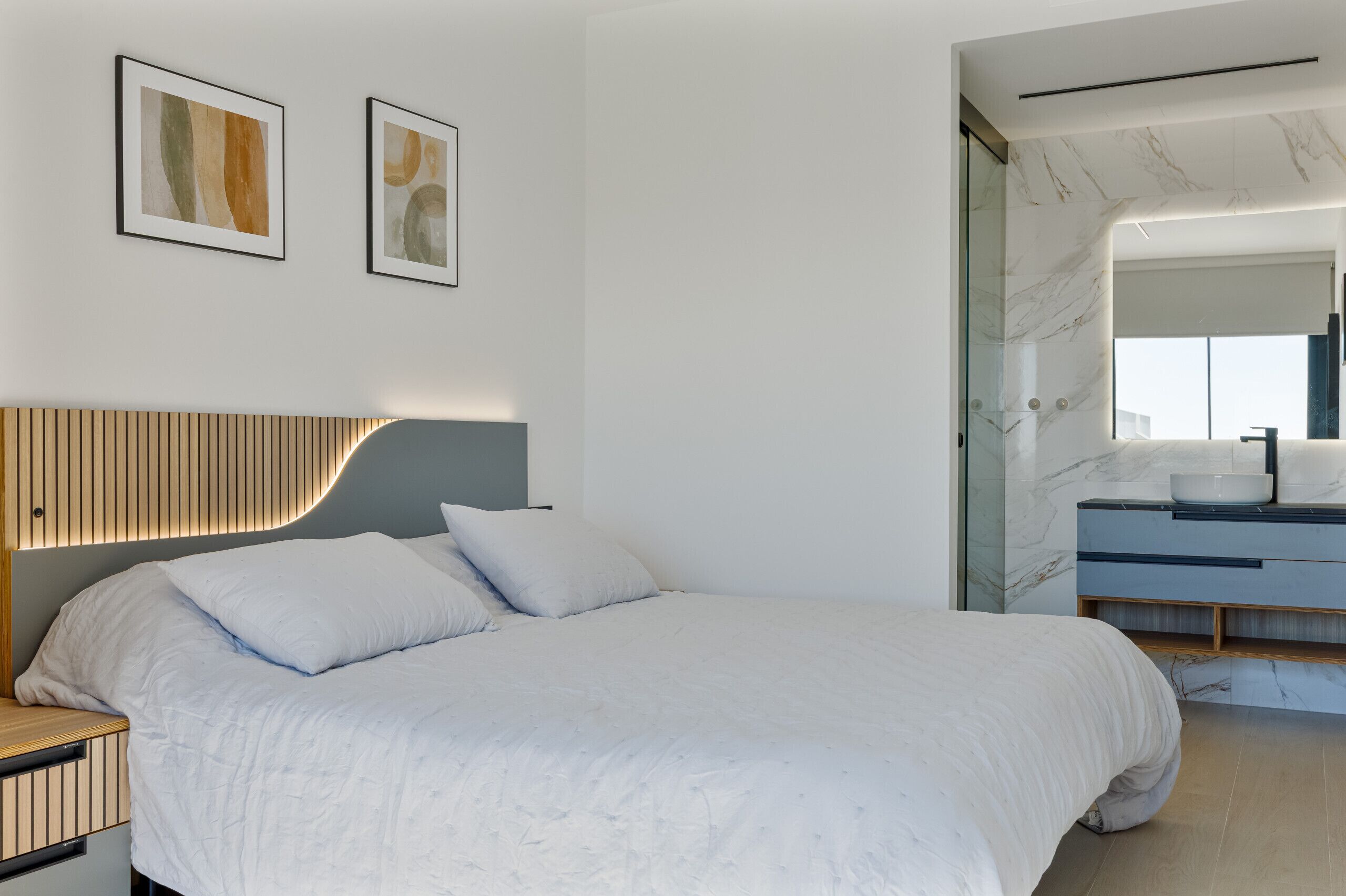 A modern bedroom with a bed, a bedside table, a mirror, and artwork on the wall.