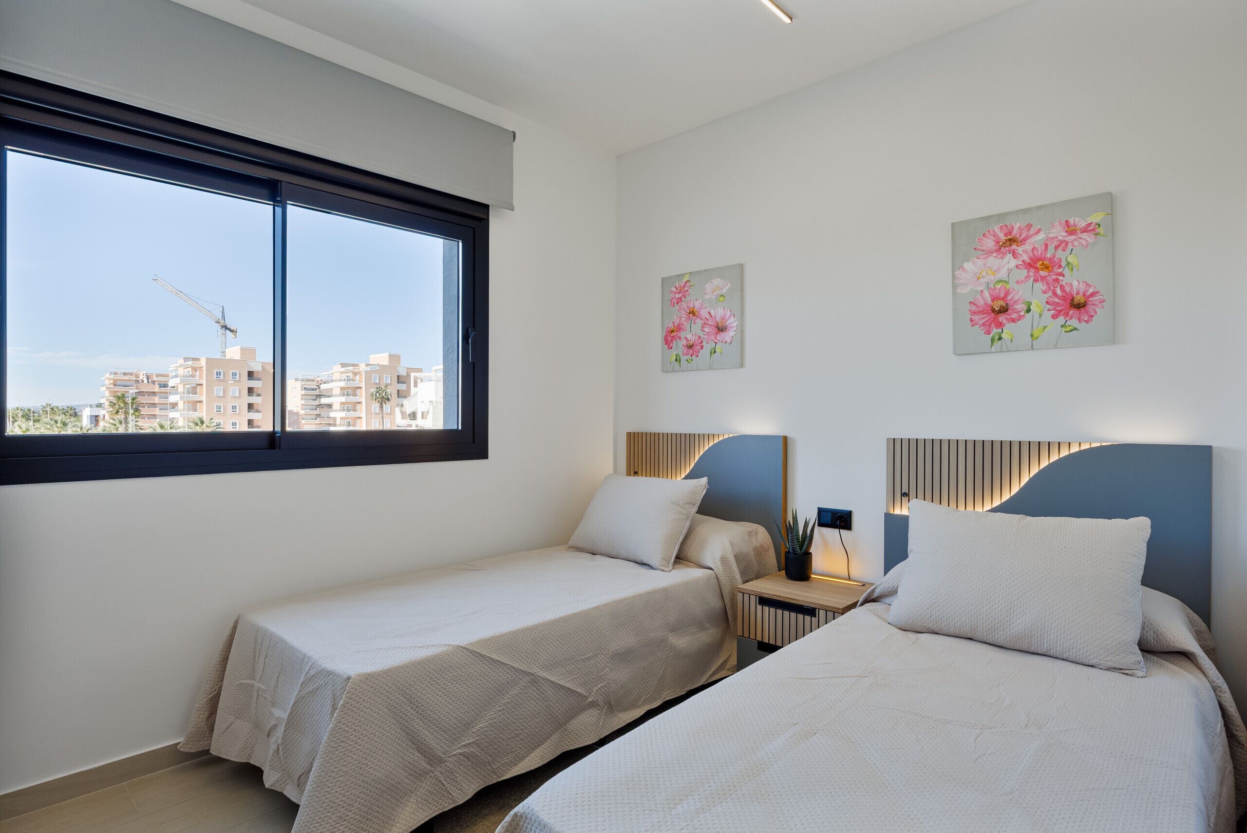A hotel room with two beds, a large window, and artwork on the walls.