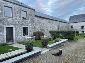 A stone building with a paved courtyard, a small table and chairs, and a dog on the cobblestone path. - Room-private Room With Shared Bathroom (Clavier)
