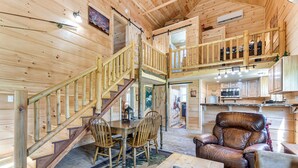 A wooden cabin interior with a dining area, a leather chair, and a staircase leading to a loft. - Hobbit House & Creekside Cabin on 6 Acres in Cosby (Cosby)