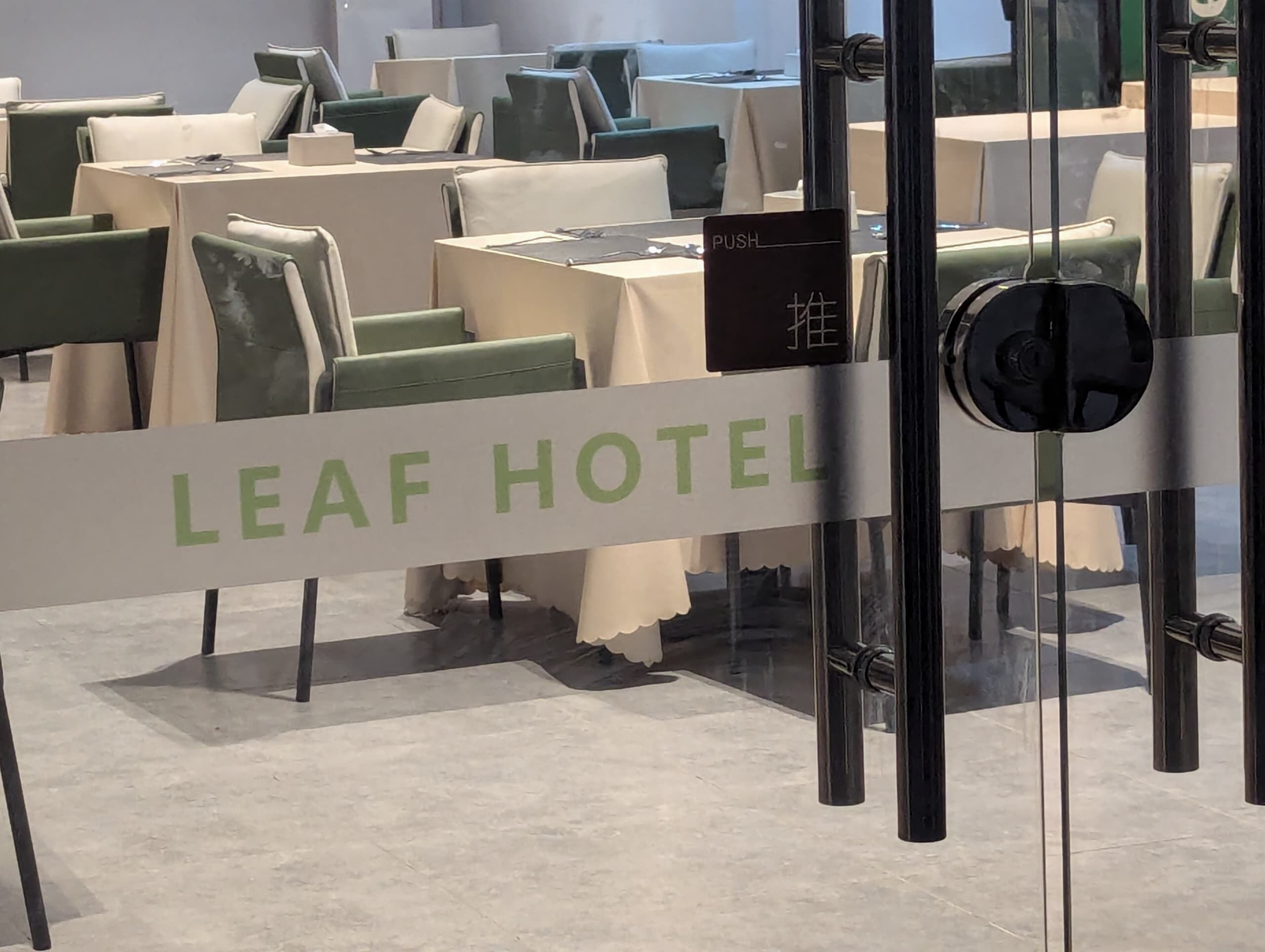 A hotel interior with tables and chairs, a sign indicating a push service, and a glass partition with the hotel's name.