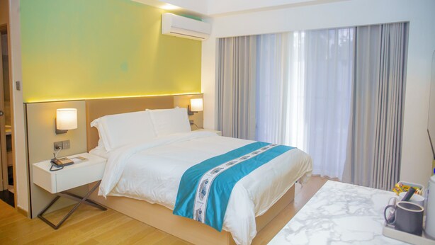 Una habitación de hotel con cama, mesitas de noche, aire acondicionado, ventana con cortinas y una mesa de centro con una taza.