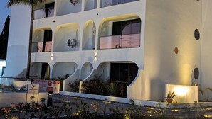 Un edificio moderno de varios pisos con balcones, iluminación exterior y un letrero de piso mojado.