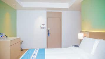 Una habitación de hotel con cama, mesita de noche, lámpara y una puerta con panel de control.