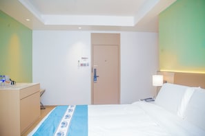 Una habitación de hotel con cama, mesita de noche, lámpara y una puerta con panel de control.
