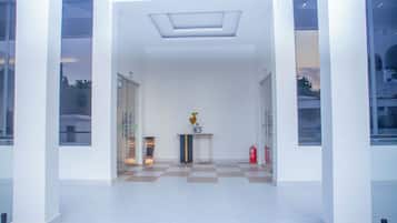 A modern lobby with a checkered floor, a central table with a vase, and glass doors leading to other areas.
