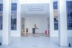 Un vestíbulo moderno con suelo a cuadros, una mesa central con un jarrón y puertas de vidrio que dan a otras áreas.