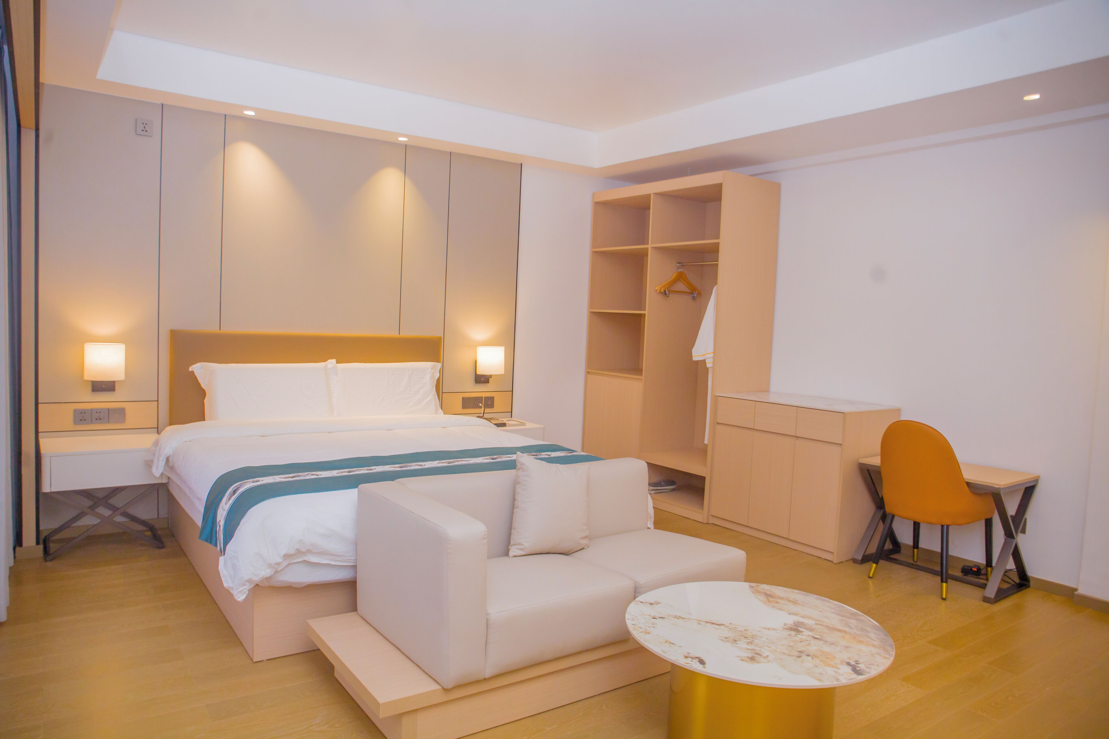 A modern hotel room with a bed, a sofa, a desk, and a wardrobe.