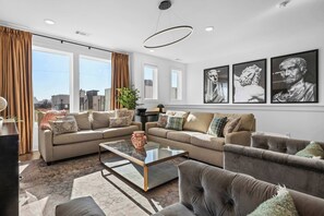 Ein modernes Wohnzimmer mit einem Ecksofa, einem Glastisch und einem großen Fenster mit Vorhängen.