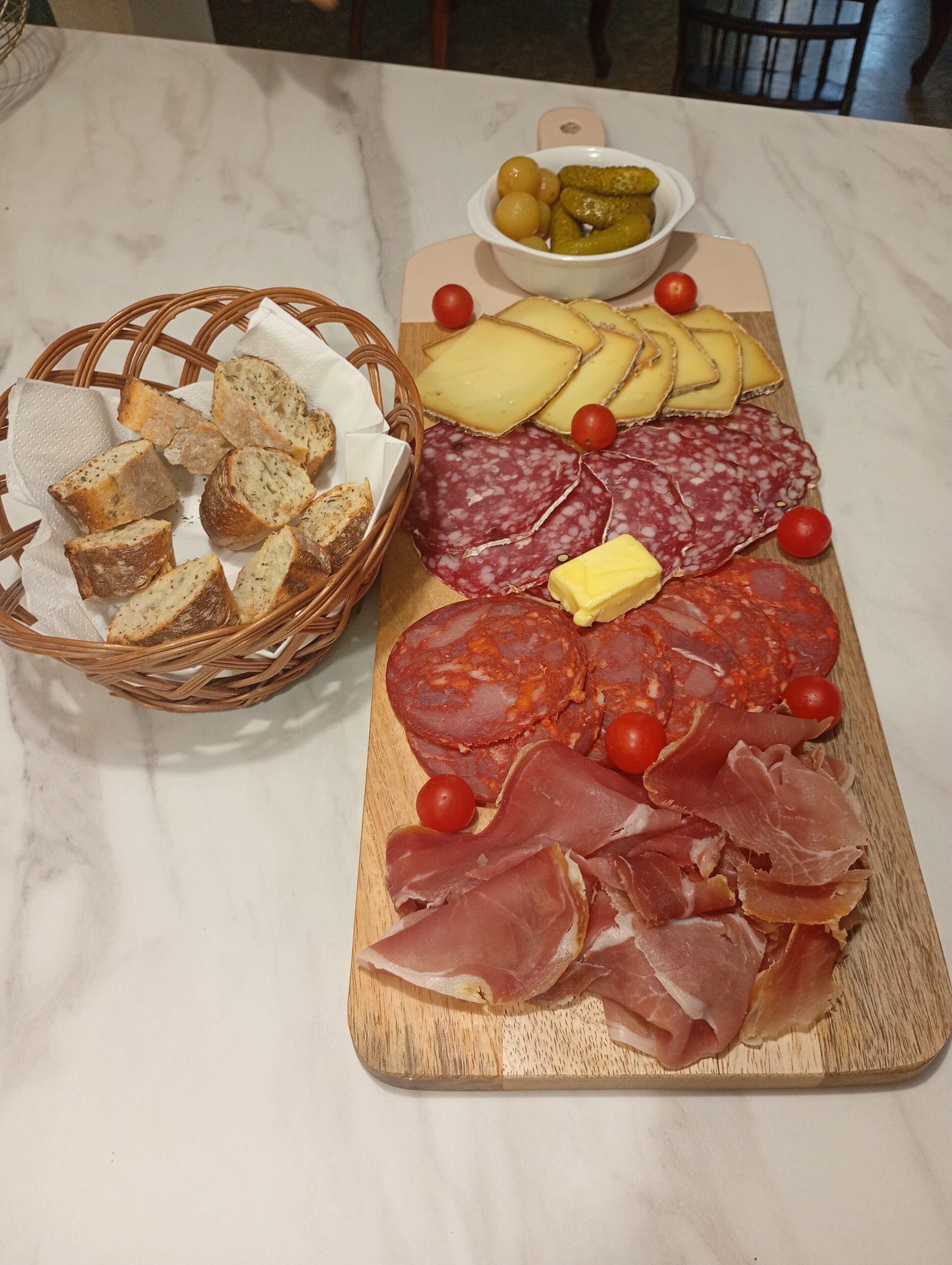 A charcuterie board with various meats, cheeses, and pickles on a marble table.
