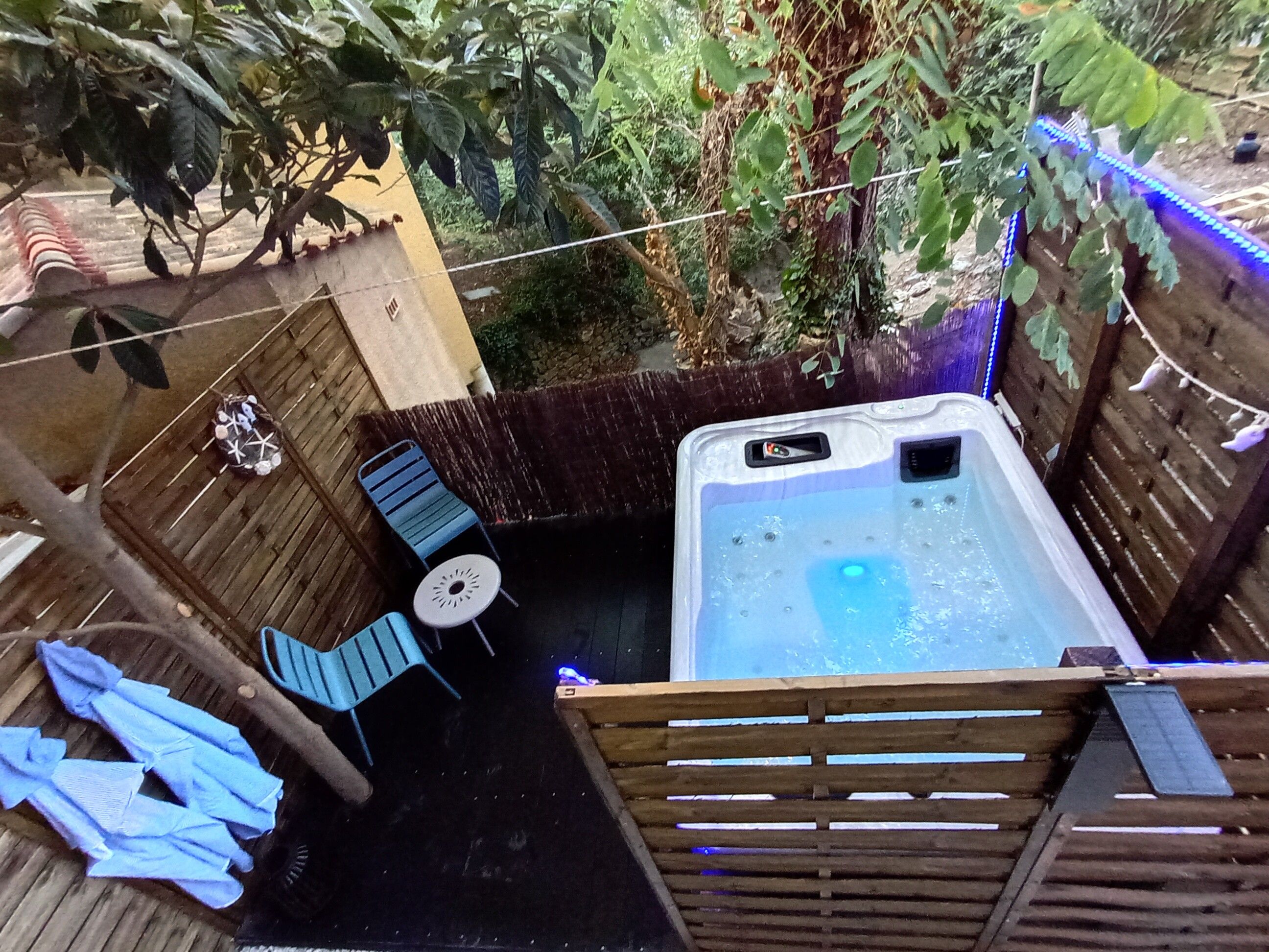 Een hottub omringd door een houten terras, een tafeltje met stoelen en een bamboe hek.
