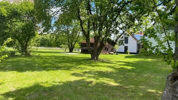 A grassy yard with a large tree, a white building with a brown roof, and a wooden fence.