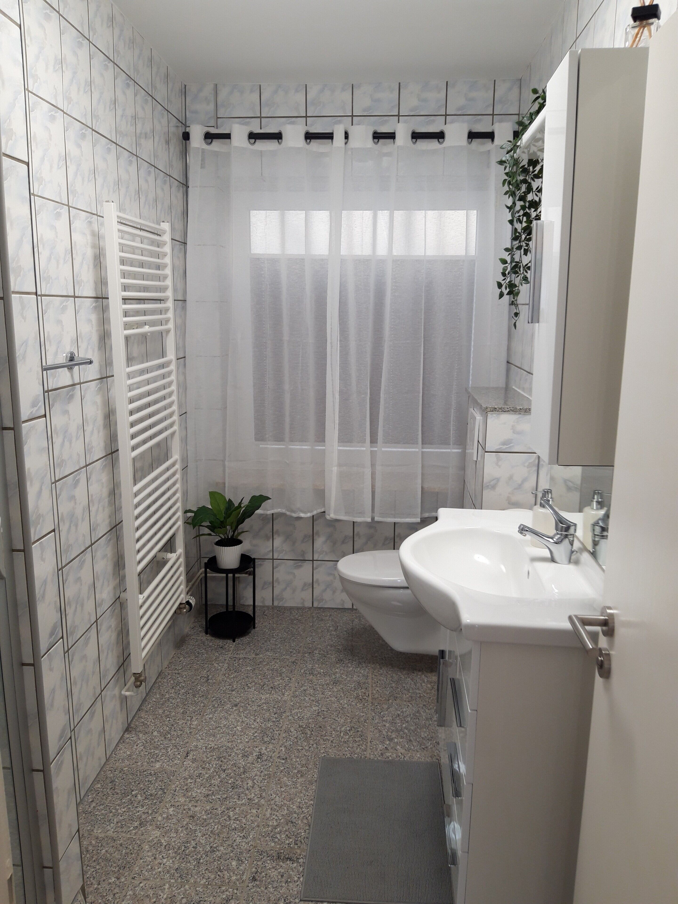 A bathroom with a toilet, sink, shower curtain, radiator, and a potted plant.