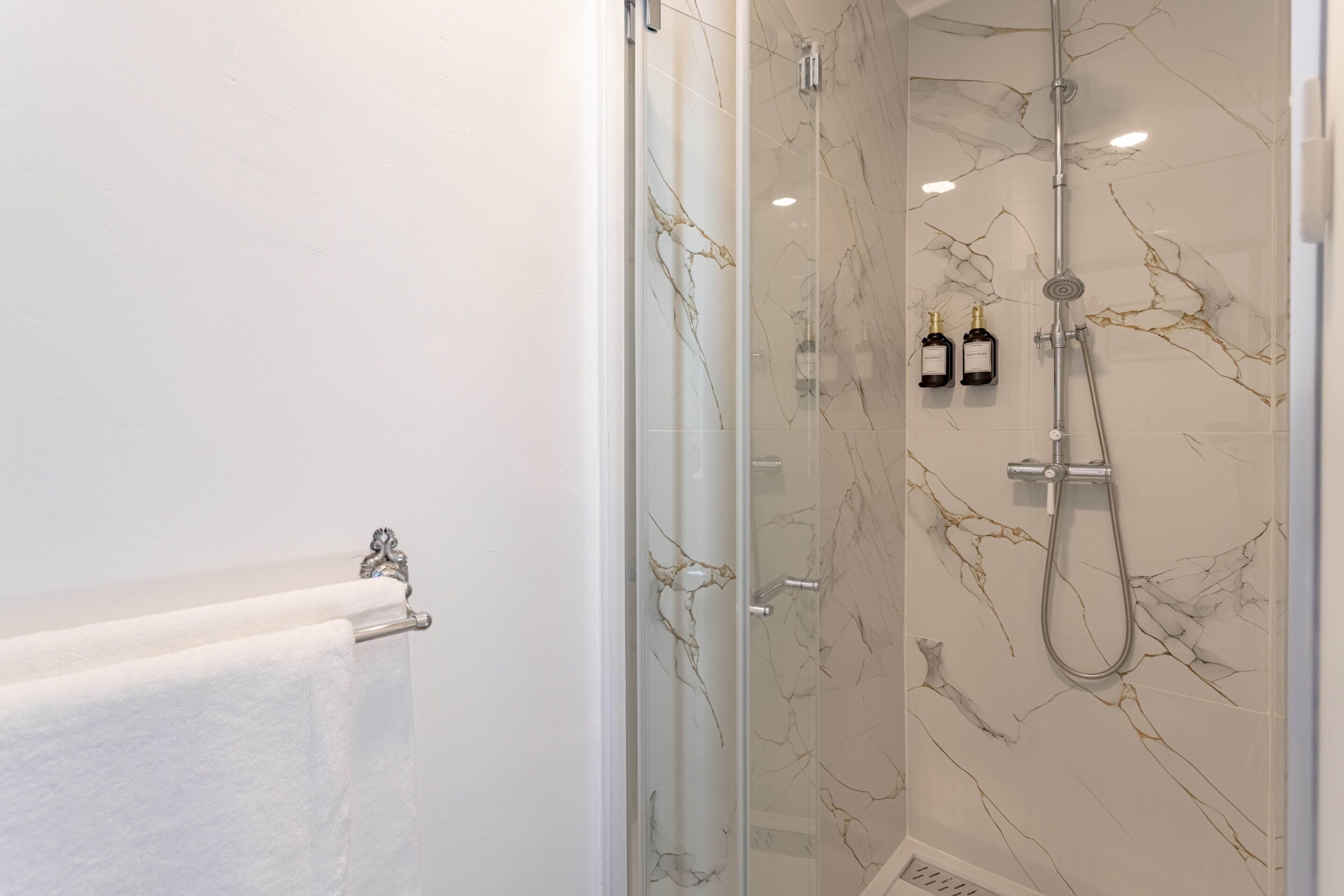 Une salle de bain moderne avec une douche à parois de verre, des murs en marbre et un porte-serviettes.