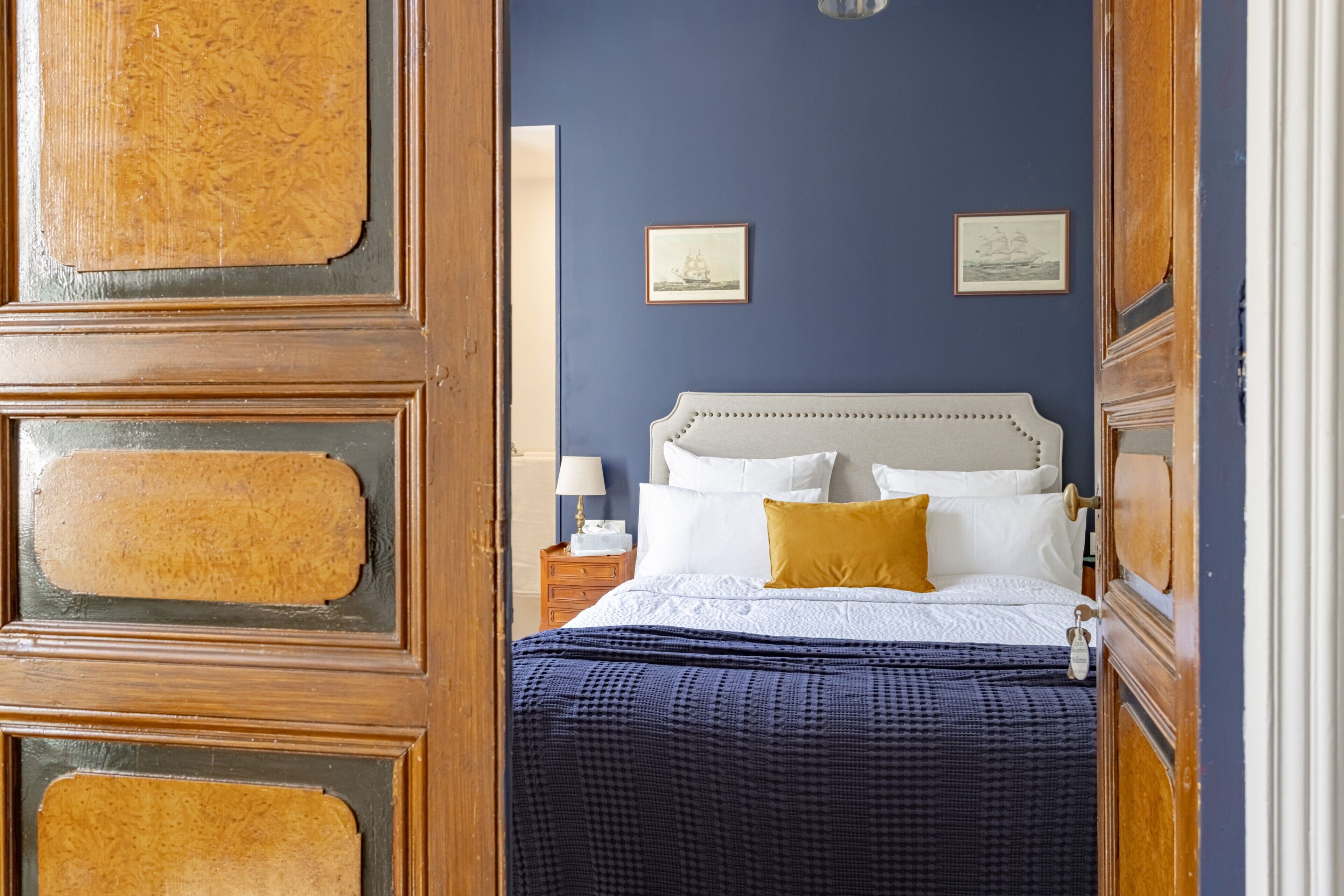 Een slaapkamer met een bed, een nachtkastje, een lamp en twee foto's in een lijst aan de muur.