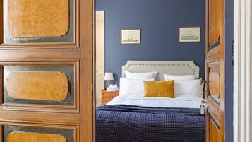 Een slaapkamer met een bed, een nachtkastje, een lamp en twee foto's in een lijst aan de muur.