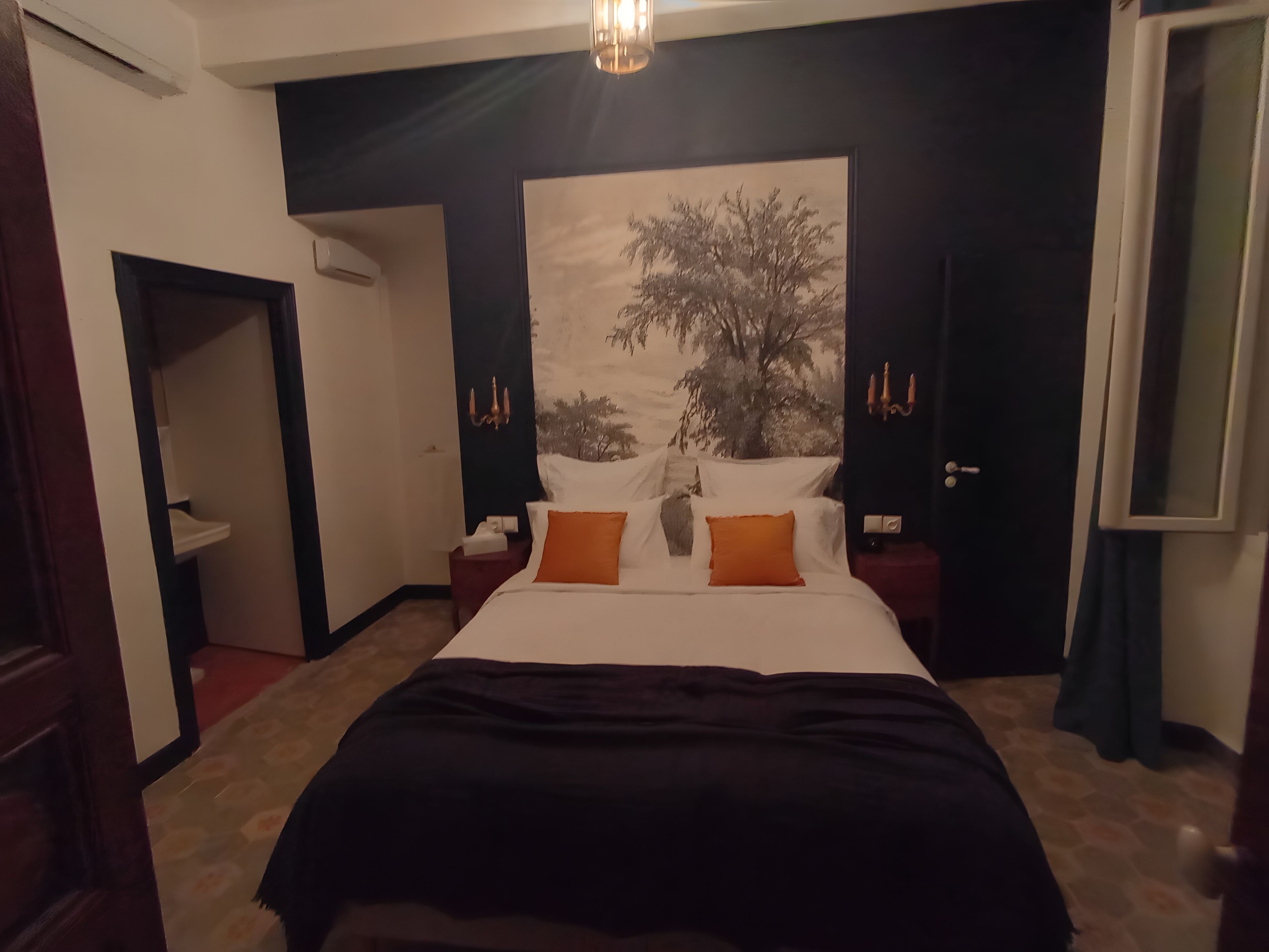 Una habitación de hotel con una cama grande, una mesita de noche, una lámpara de pared y una puerta.