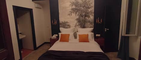 Una habitació d'hotel amb un llit gran, una tauleta de nit, una làmpada de paret i una porta.