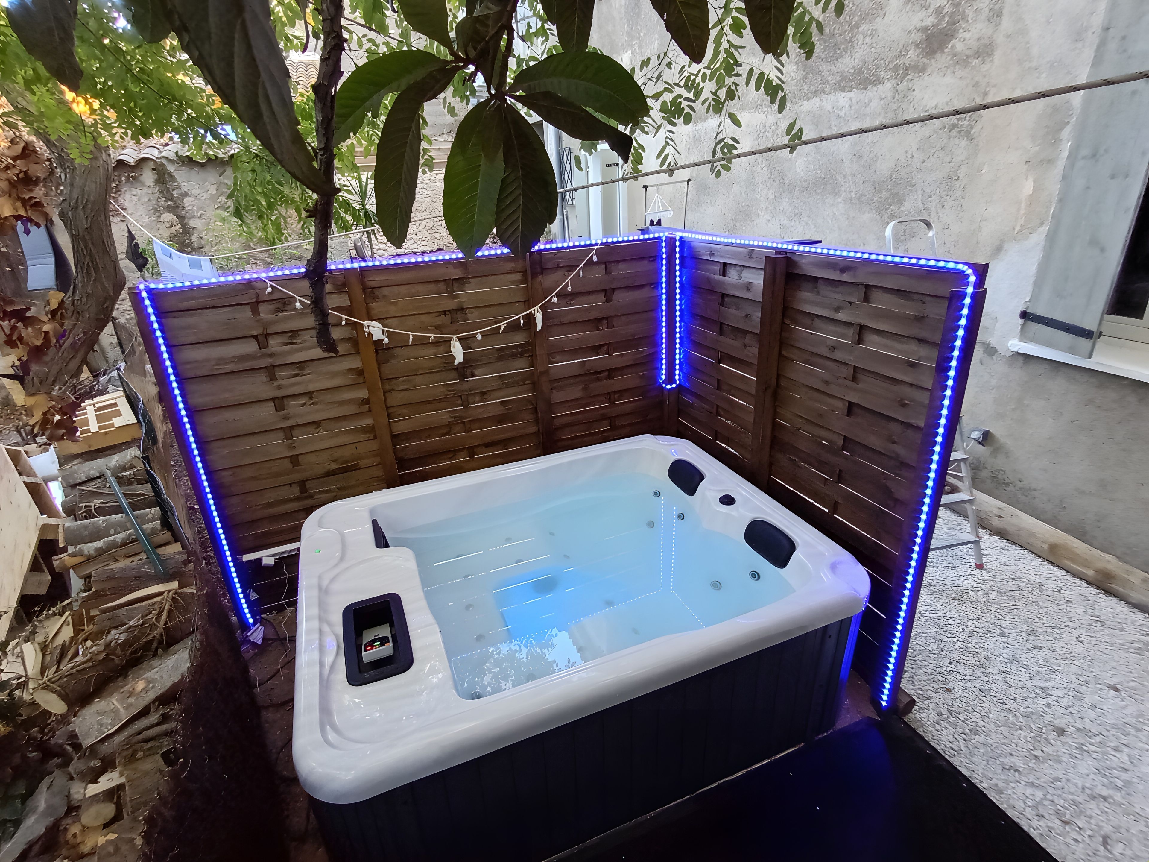 Ein Whirlpool mit LED-Beleuchtung, umgeben von Holzwänden und einem Baum.