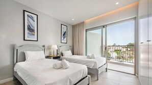 Hotellihuone, jossa on kaksi sänkyä, yöpöytä lampulla, suuri ikkuna, josta on näkymä, ja lasiliukuovi parvekkeelle.