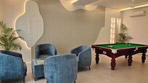 Una mesa de billar con superficie de fieltro verde, dos sillones azules y una pared con líneas verticales y un diseño abstracto grande.
