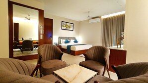 A hotel room with a bed, two armchairs, a coffee table, a desk, and a mirror. - Radiance Hotel (Sirsa)