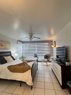 Ein Hotelzimmer mit Bett, Schreibtisch, Stuhl, Fernseher und Deckenventilator.
