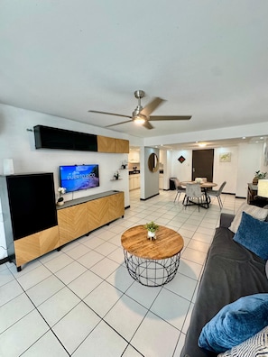Ein modernes Wohnzimmer mit Fernseher, Sofa, Couchtisch und Deckenventilator.