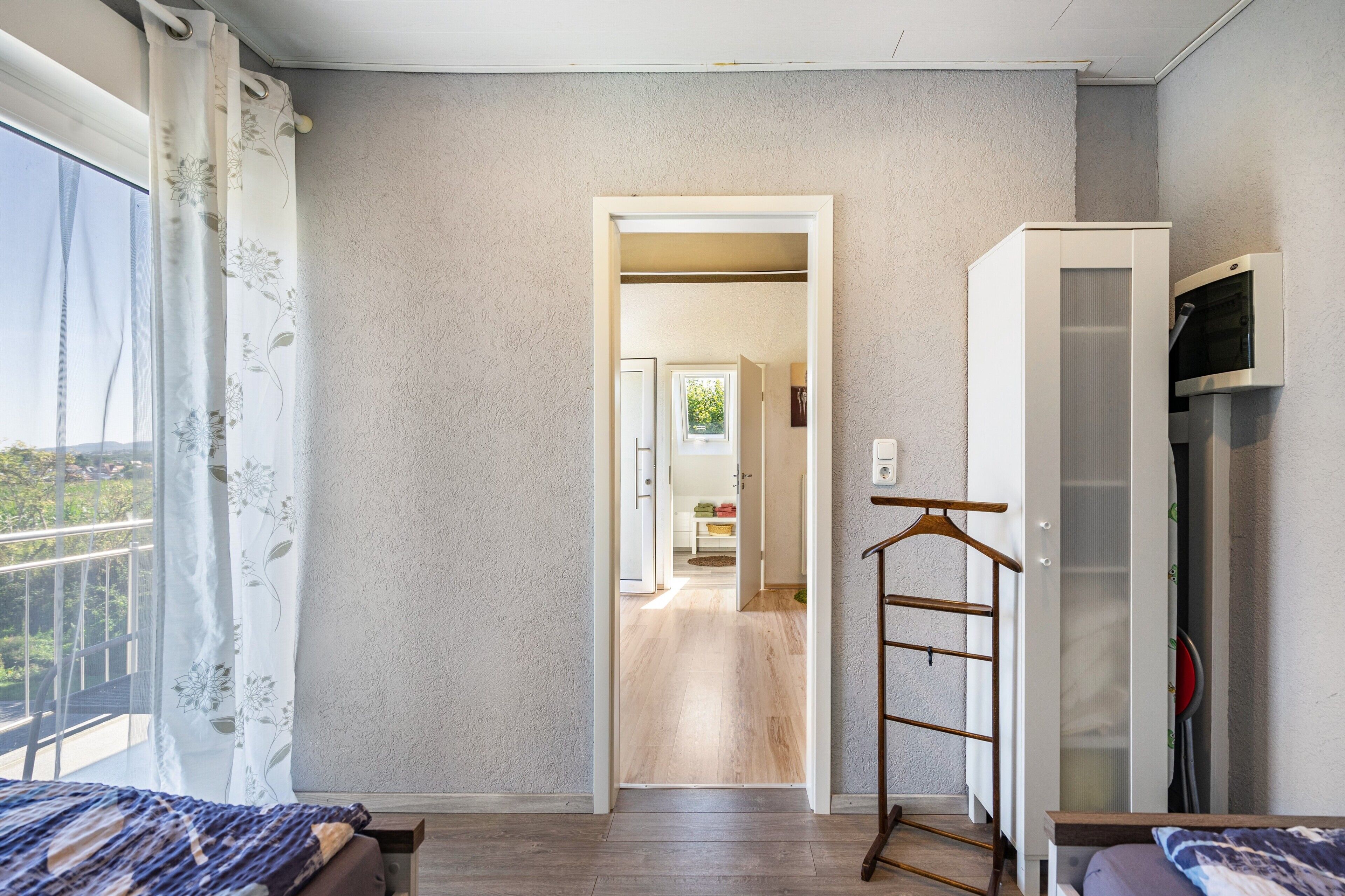 Une chambre avec un lit, une armoire, un portant et une vue sur un balcon.