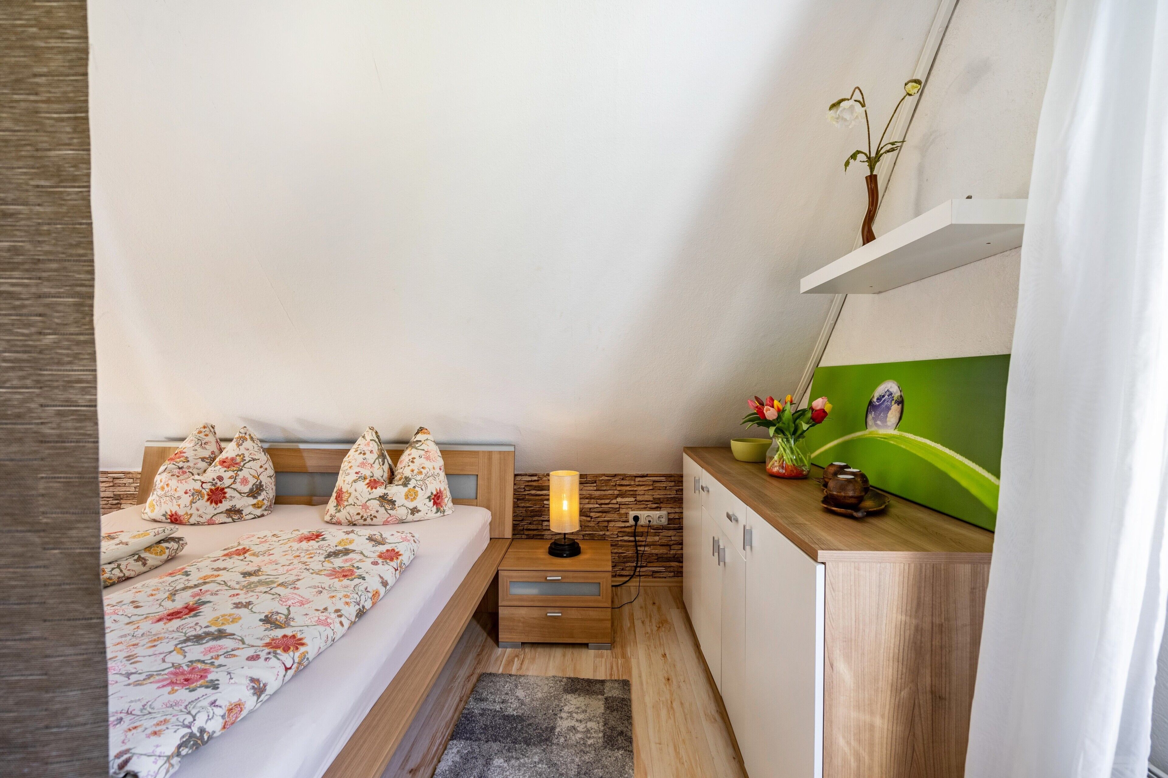 A bedroom with a bed, pillows, a nightstand, a lamp, a dresser, and a green wall.