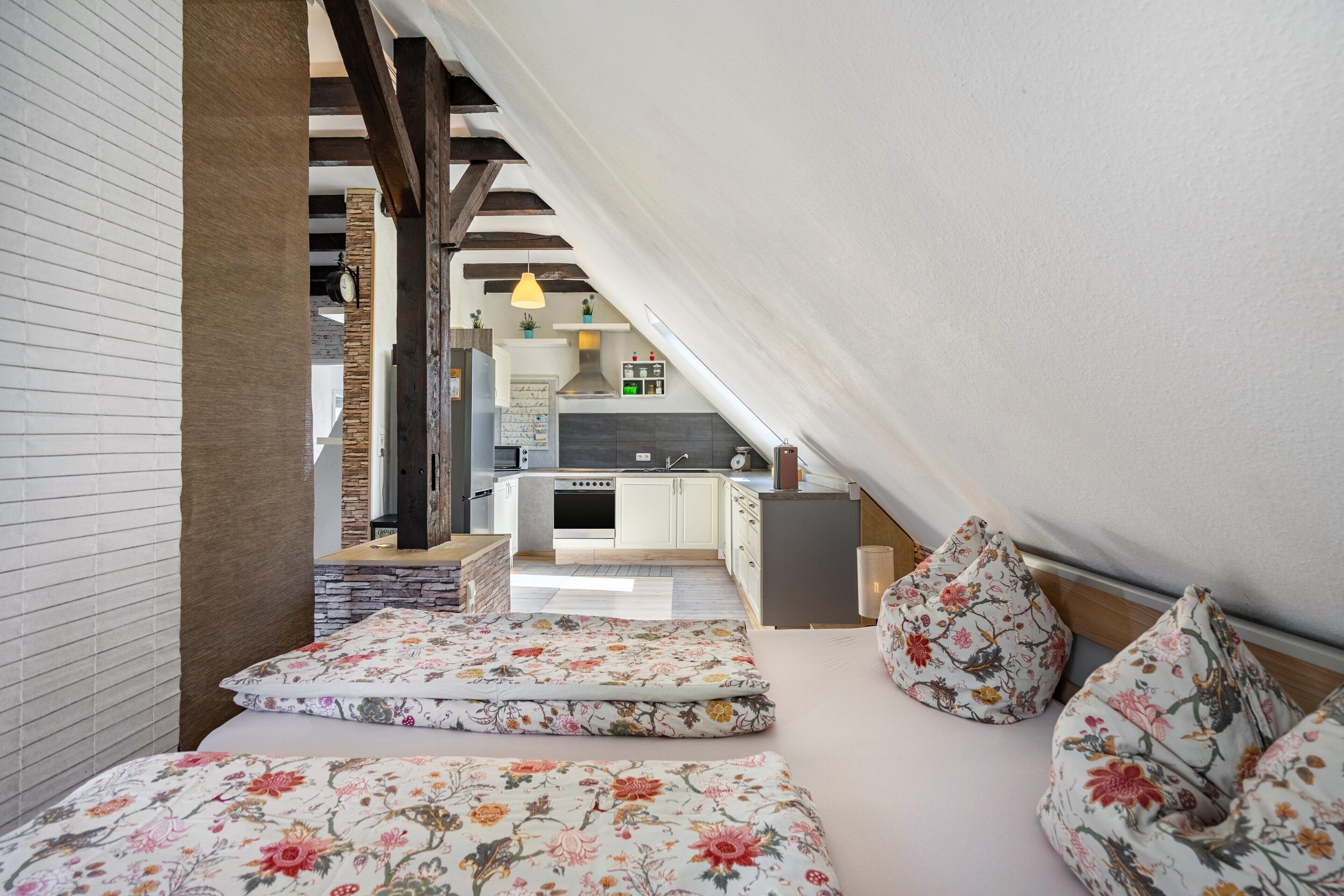 A bedroom with a bed, pillows, and a view of a kitchen and living area.