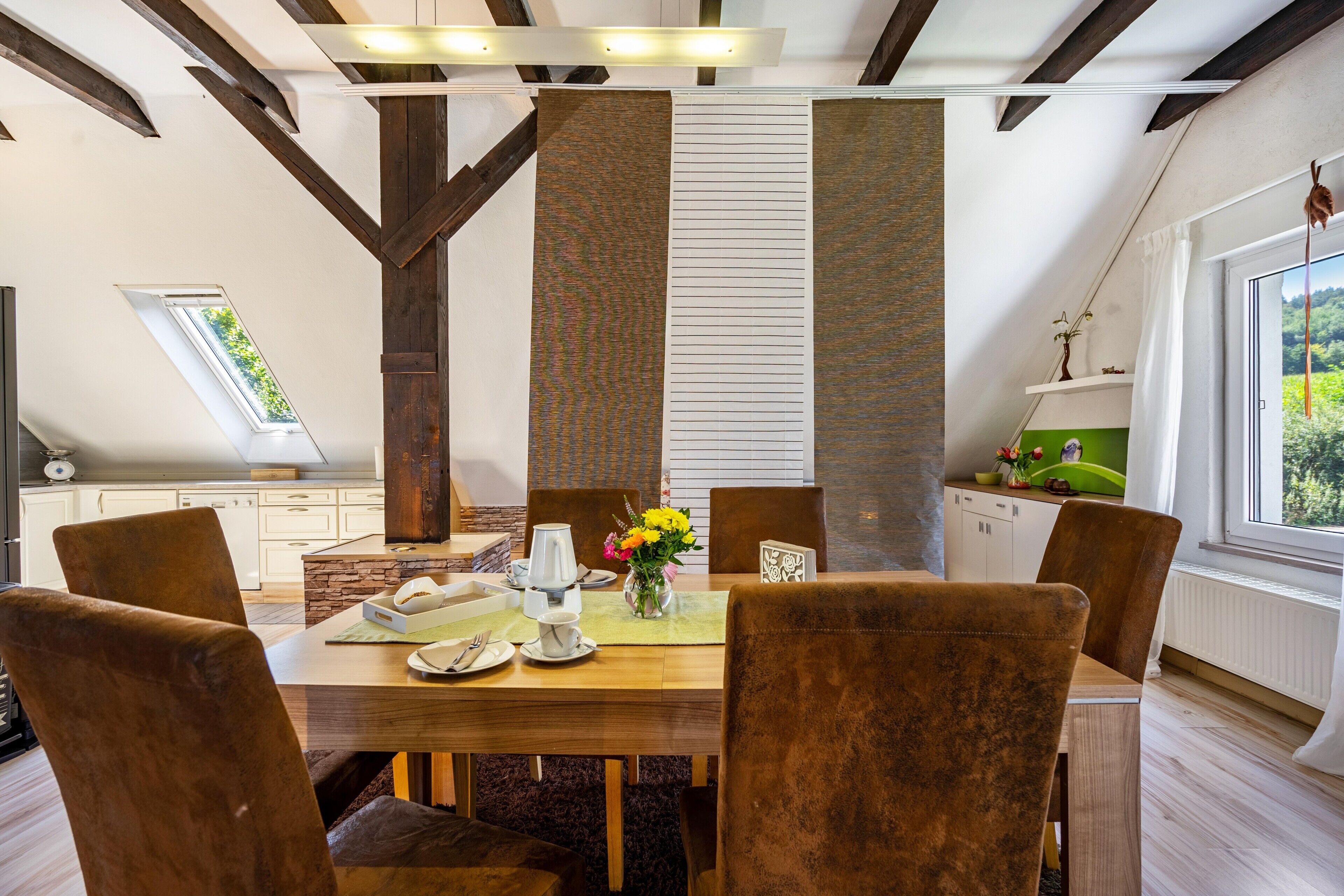 Un comedor con una mesa de madera, seis sillas y un florero con flores.