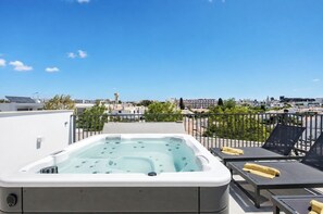 Eine Dachterrasse mit Whirlpool, Liegestühlen und Blick auf die Stadt.