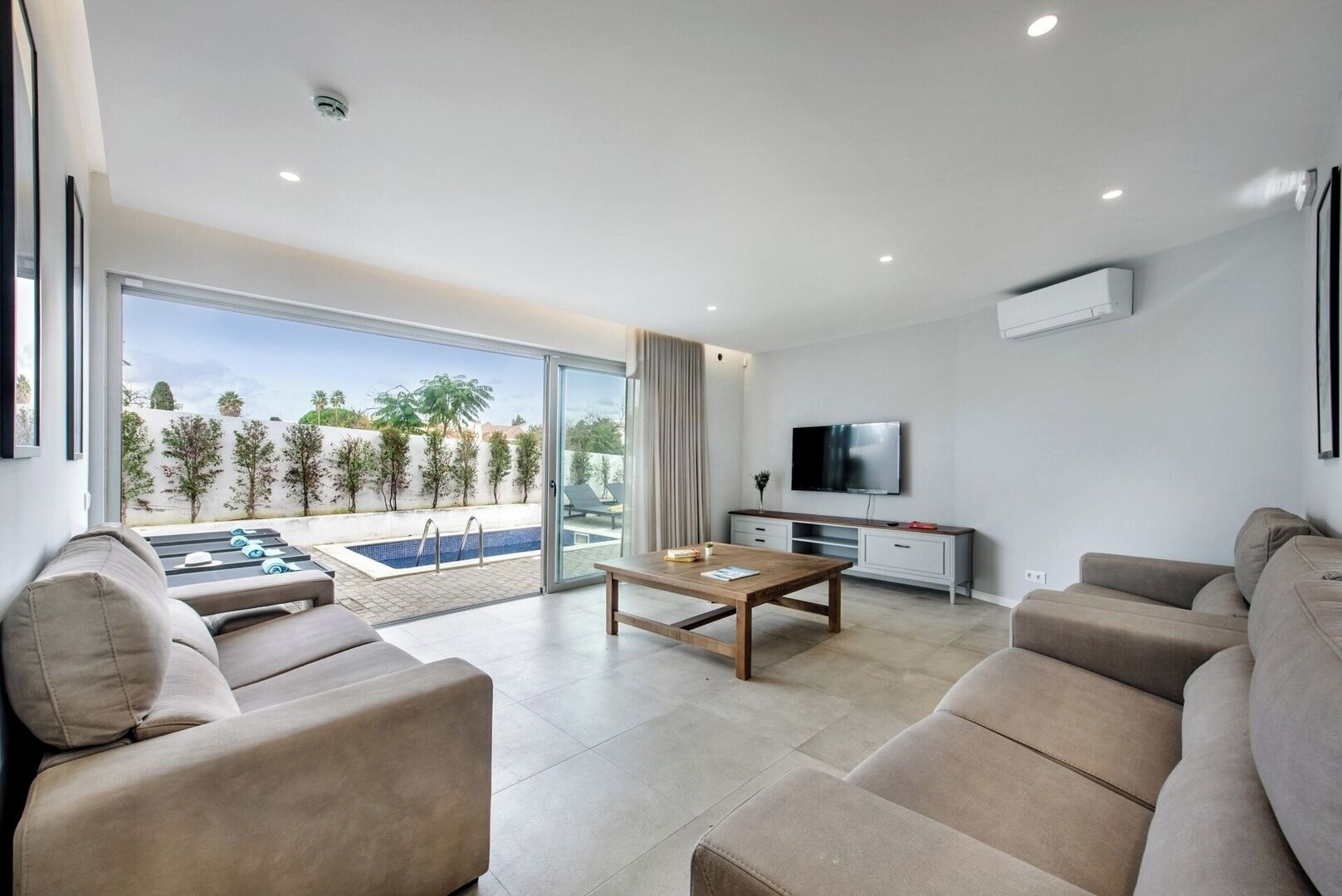 Un moderno salón con vistas a la piscina, un televisor de pantalla plana y un sofá.