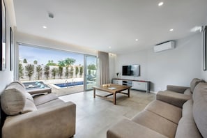 A modern living room with a pool view, a flat-screen TV, and a sofa. - Luxury Strip Villa Magnolia w/ Hot Tub, Albufeira (Albufeira)