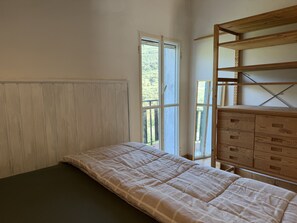 Una habitación con una cama, un aparador de madera y una ventana con vistas al verdor.