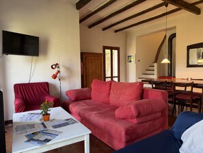 A living room with a red sofa, a white coffee table, a TV, and a dining area with a wooden table and chairs. - Retreat Zerbo Viesci (Chiusavecchia)
