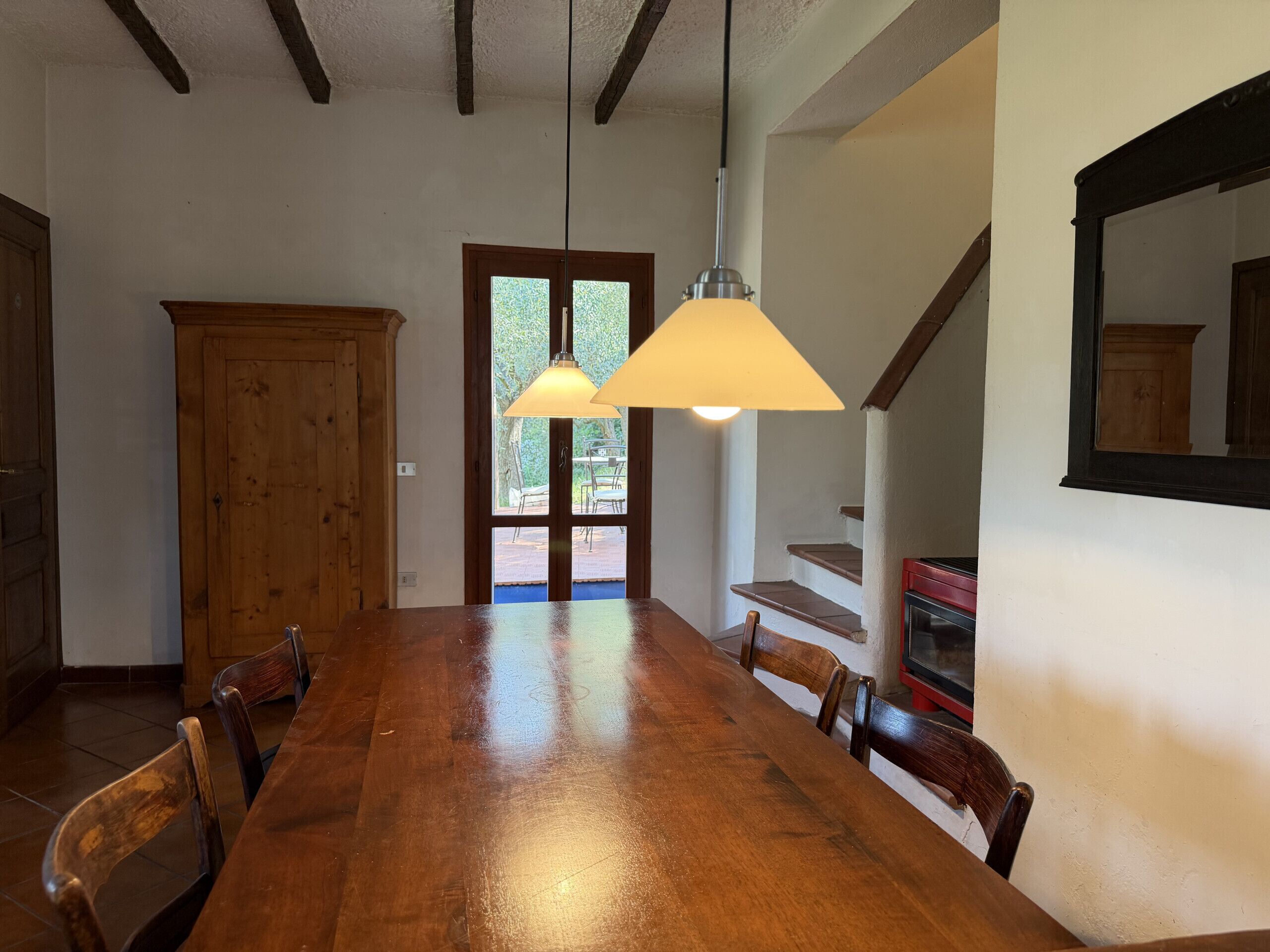 A dining area with a wooden table and chairs, a wooden cabinet, and a staircase with a red appliance.